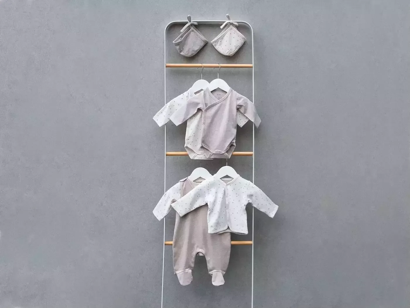 Baby-kleidungen drei hängen an einem kleiderständer.