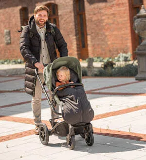 Ein Mann schiebt einen Kinderwagen, in dem ein Kind mit einem warmen Fußsack sitzt.