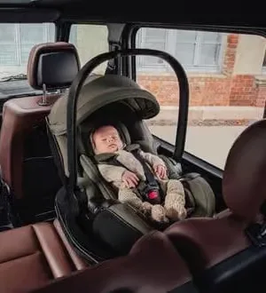 Ein schlafendes Neugeborenes liegt sicher angeschnallt in einer rückwärtsgerichteten Babyschale auf dem Rücksitz eines Autos.