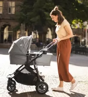 Eine Frau schiebt einen modernen Kombi-Kinderwagen.