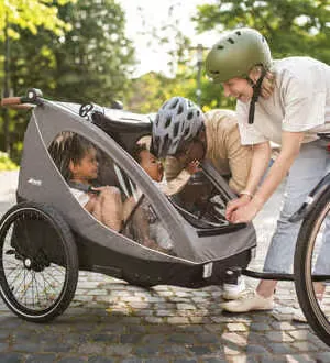 Zwei Kinder sitzen gemütlich in einem Fahrradanhänger.
