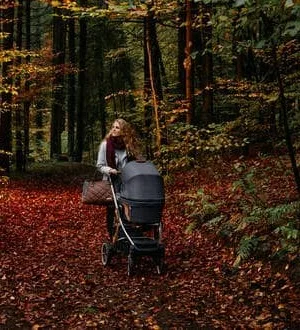 Eine Frau schiebt einen Kombi-Kinderwagen über einen Waldweg.