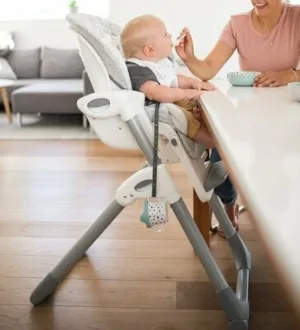 Ein Baby wird in einem zusammenklappbaren Hochstuhl am Küchentisch gefüttert.
