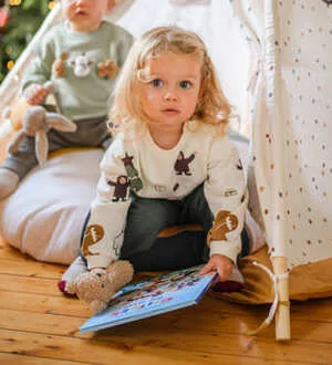 Ein kleines Mädchen sitzt mit einem interessanten Buch vor einem Spielzelt.