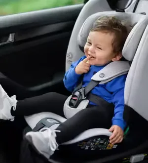 Ein Kleinkind sitzt lächelnd in einem vorwärtsgerichteten Kindersitz im Auto.