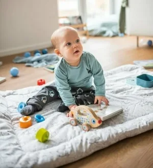 Ein Baby sitzt auf einer gepolsterten Krabbeldecke und spielt.