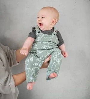 Ein lachendes Baby in einer weichen Latzhose mit süßem Muster.