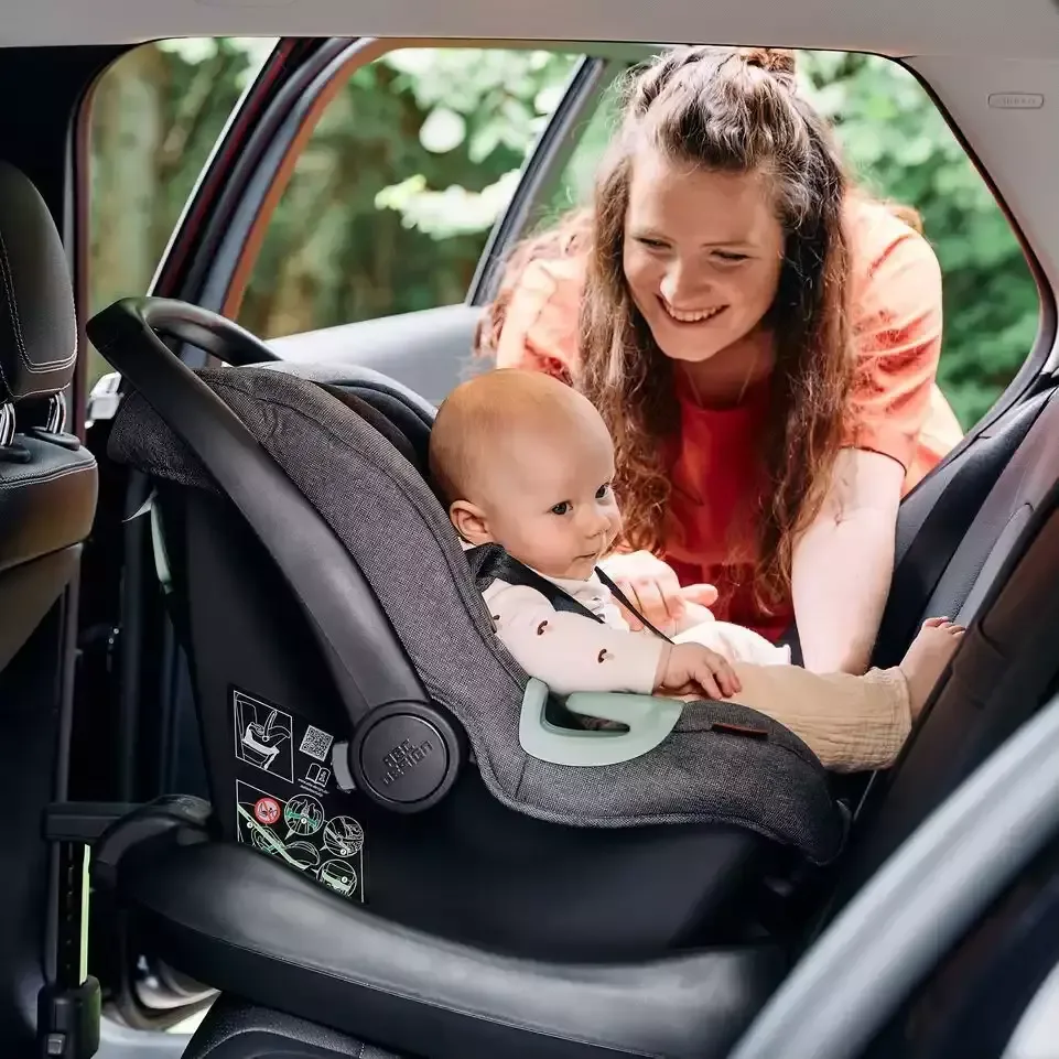 Eine frau, die ein baby auf einem autositz hält.