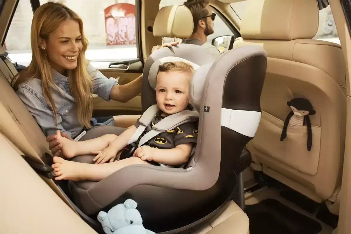 Eine frau, die ein baby auf einem autositz hält.