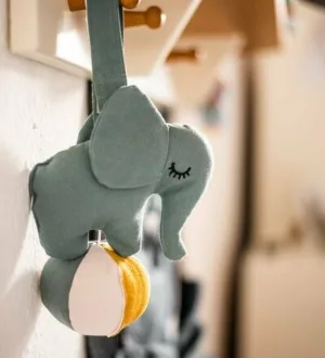 Ein weicher Greifling in Form eines grauen Elefanten mit einer kleinen Glocke hängt an einer Halterung.