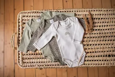 Korb ein mit babykleidung auf einem holzboden.