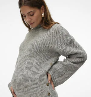 Einer schwangere Frau in einem grauen Grobstrickpullover mit seitlicher Knopfleiste.