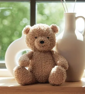 Ein klassischer, weicher Teddybär sitzt dekorativ auf einer Holzoberfläche vor einem Fenster.