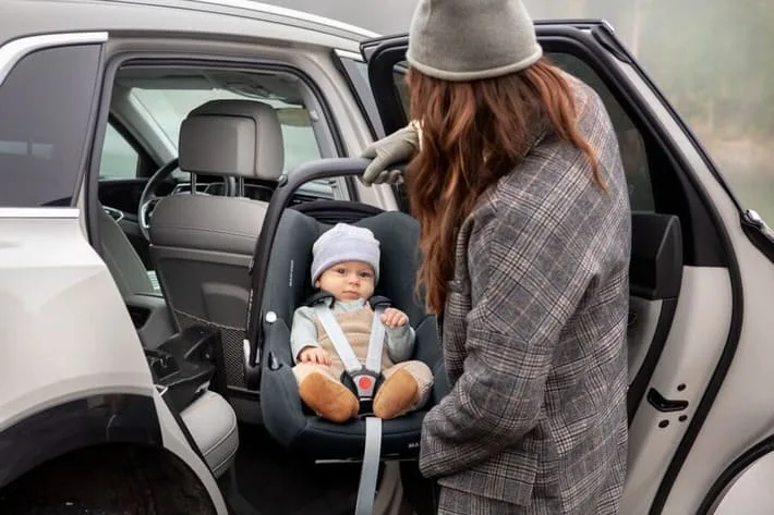 Eine frau, die ein baby auf einem autositz hält.