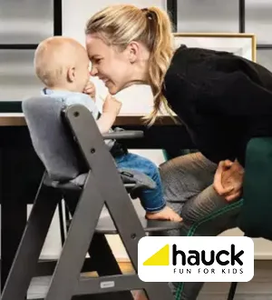 Eine Mutter lächelt ihr Kind an, das in einem Hochstuhl von Hauck am Tisch sitzt.
