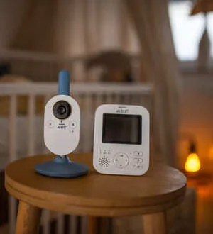 Ein digitales Video-Babyphone steht auf einem Holzhocker in einem abgedunkelten Kinderzimmer.