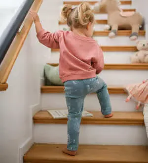 Ein Kleinkind in gemusterten blauen Leggings klettert eine Holztreppe hinauf.