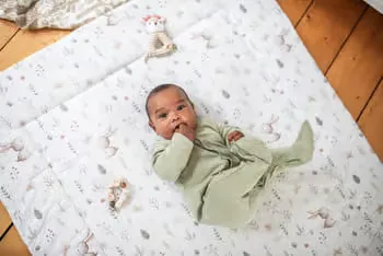 Baby ein, das auf einem bett neben einem ausgestopften tier.