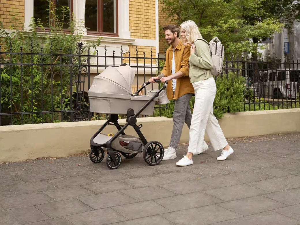 Eltern schieben den ELSA & EMIL Kinderwagen in kängurugrau durch ein Wohngebiet.