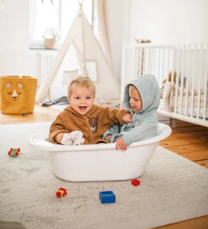 Zwei Kleinkinder sitzen in Bademänteln spielerisch in einer Wanne.