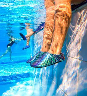 Kinderfüße mit Badeschuhe hängen im Wasser.