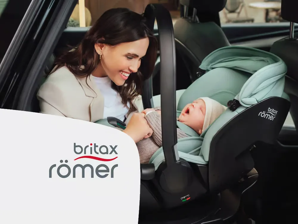 Eine frau, die ein baby auf einem autositz hält.