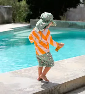 Kind läuft am Pool in UV-Schutz Bademode und Hut.