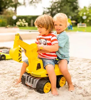 Zwei Kinder sitzen auf dem Maxi-Digger im Sandkasten.