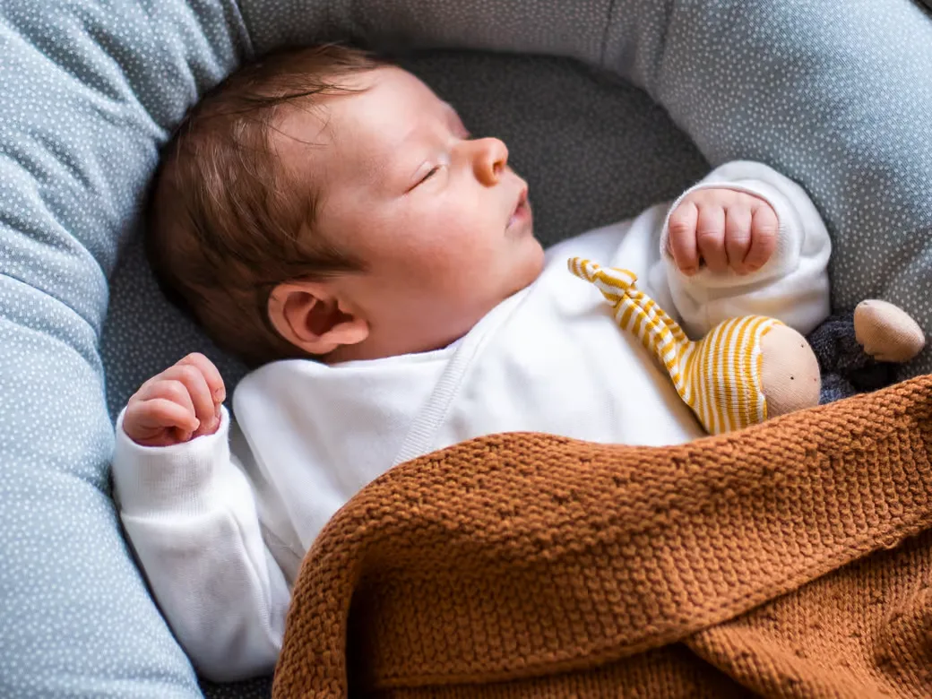 Baby schläft unter eine brauen Strickdecke.