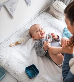 Ein lachendes Baby liegt auf einer weichen Wickelunterlage.