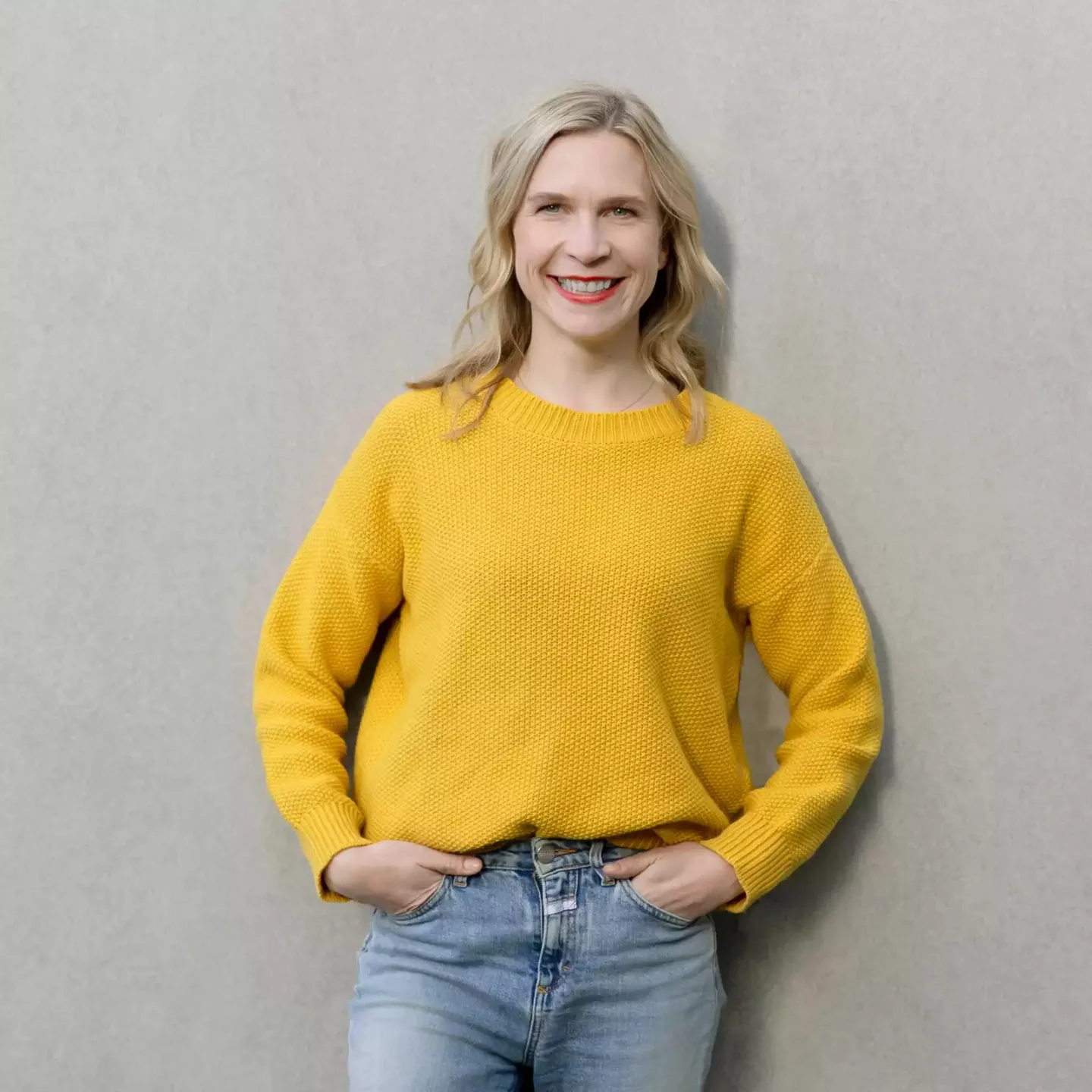 Eine frau trägt einen gelben pullover und jeans.